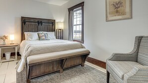 Een slaapkamer met een houten bed, een nachtkastje, een lamp, een stoel en een raam met gordijnen.