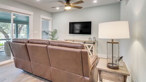 Ein modernes Wohnzimmer mit einer braunen Ledersofa, einem Deckenventilator, einem Flachbildfernseher und einer Stehlampe.