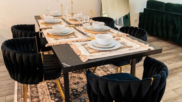 Uma sala de jantar com uma mesa comprida posta para seis pessoas, cadeiras estofadas pretas, um espelho e arte abstrata na parede.