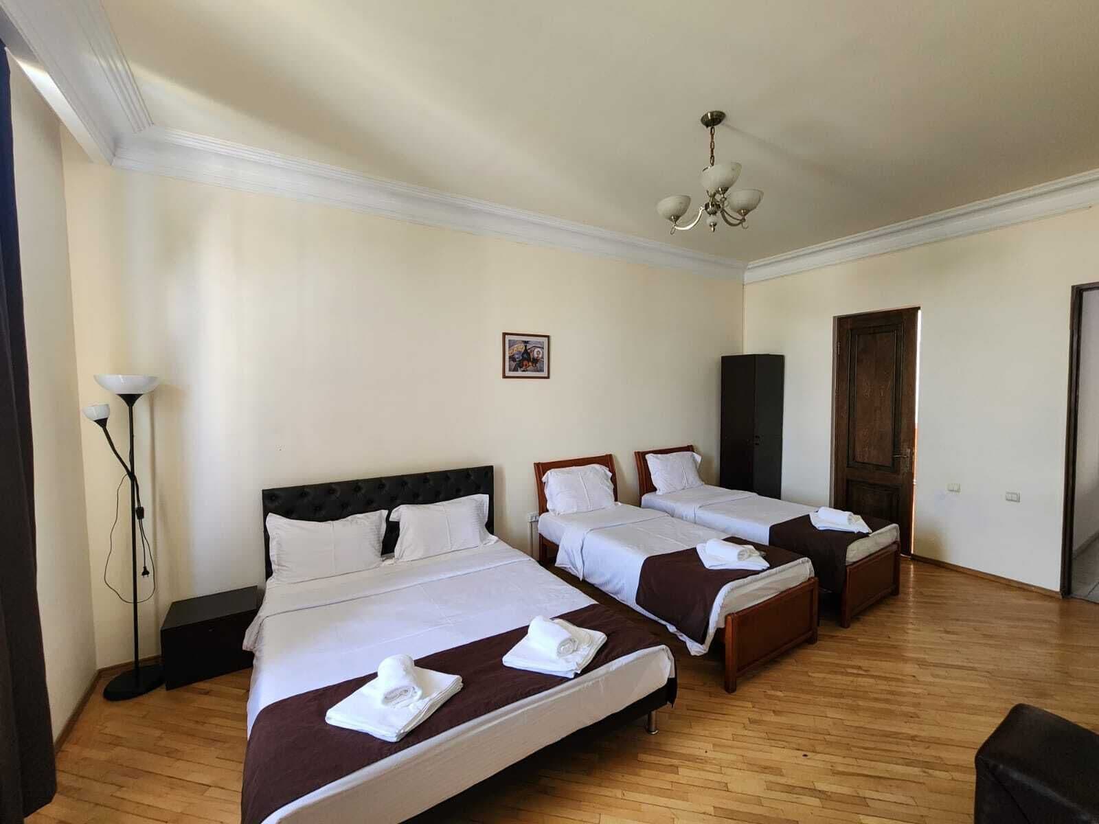 A hotel room with three beds, a chandelier, a floor lamp, and a wardrobe.