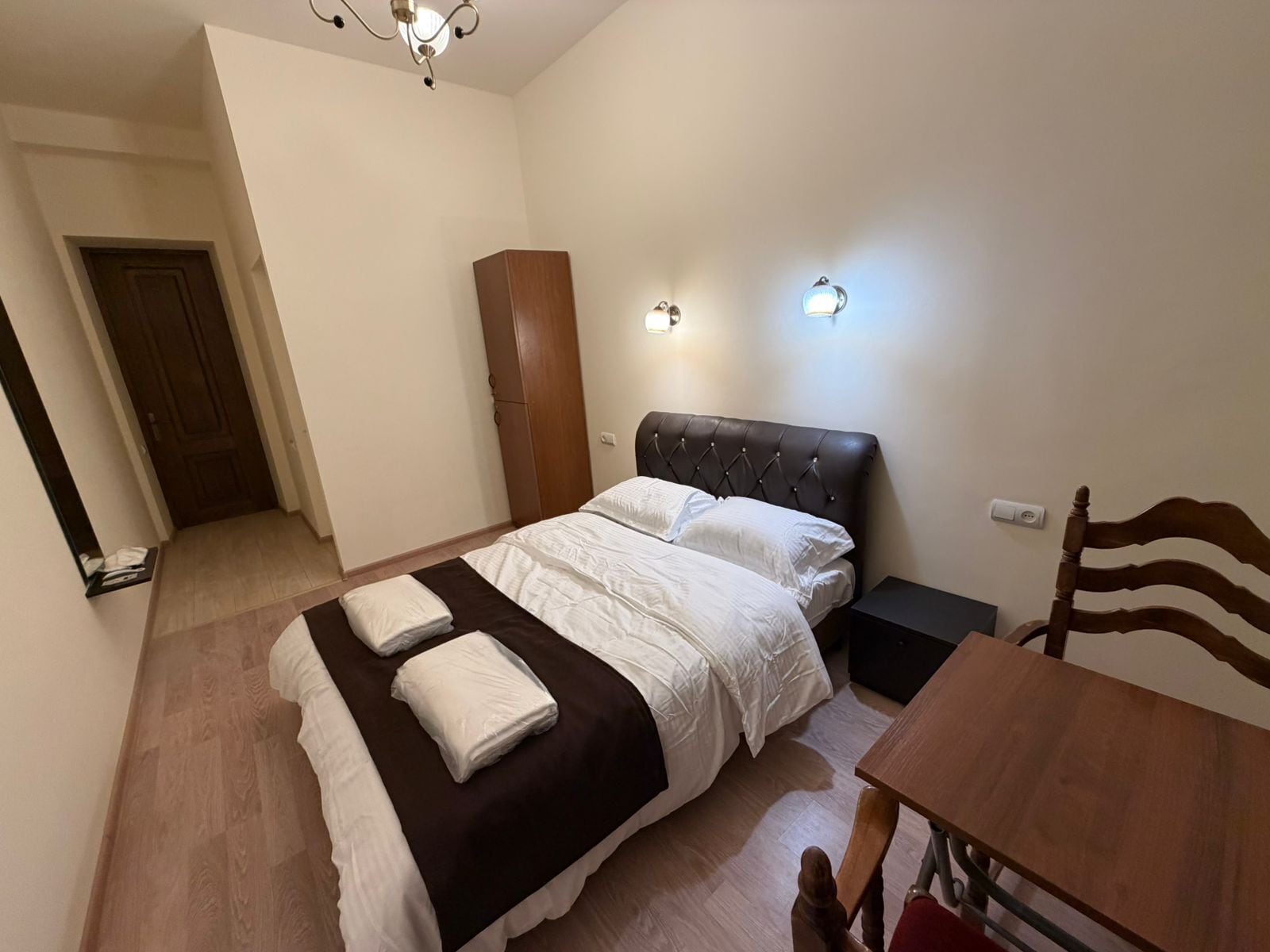 Ein Schlafzimmer mit Bett, Nachttischen, einem Holzschrank, einem Sessel und einem Tisch.