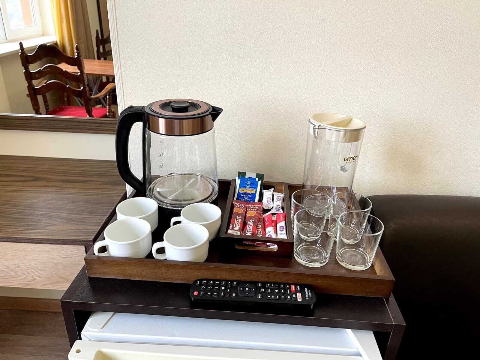 A tray with a coffee maker, cups, glasses, a remote control, and coffee packets.