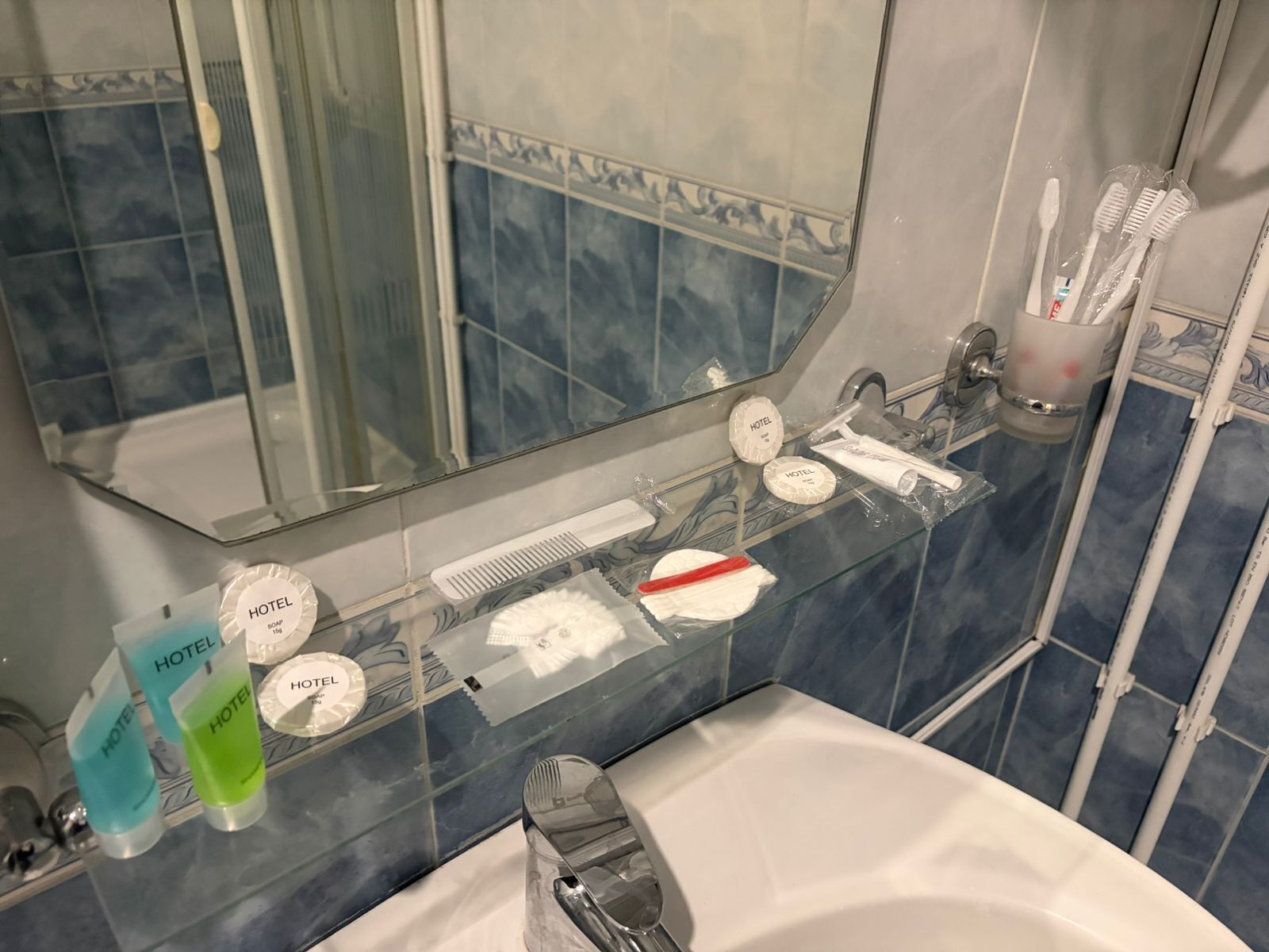 Een badkamer met glazen scheidingswand, een wastafel, een spiegel en toiletartikelen op het aanrecht.