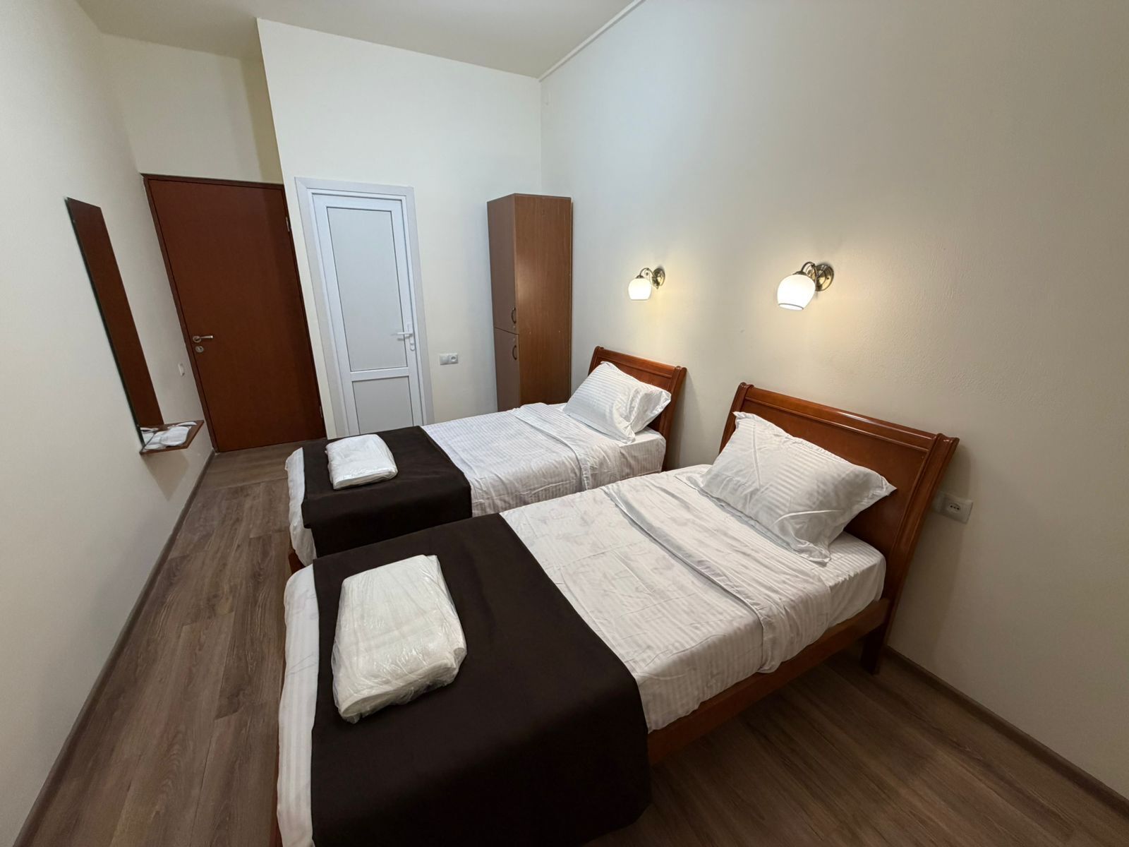 Une chambre avec deux lits, une armoire, une porte et des lampes fixées au mur.