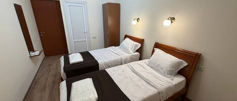 Une chambre avec deux lits, une armoire, une porte et des lampes fixées au mur.