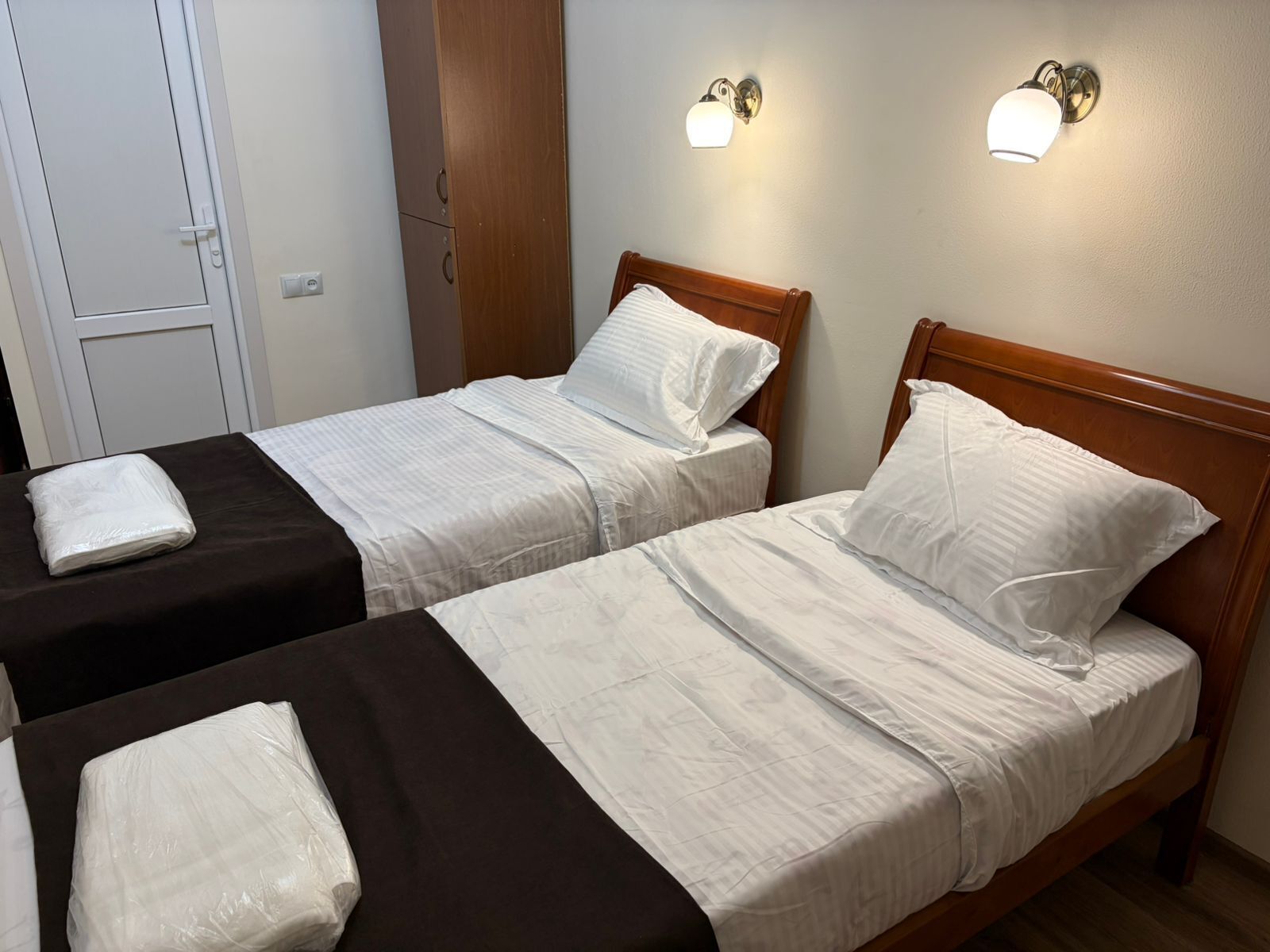 Dos camas individuales con cabeceros de madera, ropa de cama blanca y dos lámparas fijadas a la pared.