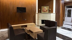 A modern living room with a fireplace, wooden paneling, a flat-screen TV, and a seating area with leather chairs and a wooden coffee table. - Nana Grand Hotel (Yerevan)