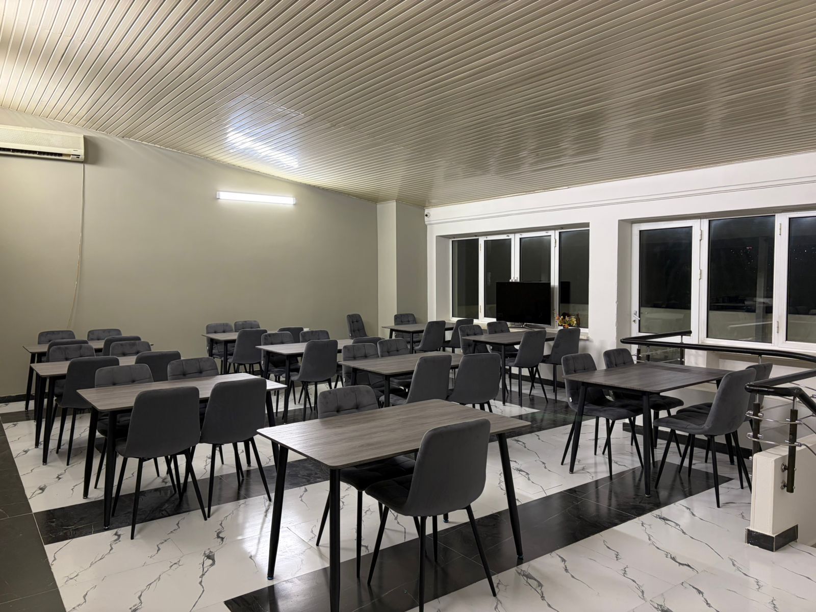 A conference room with tables and chairs, a flat-screen TV, and large windows.