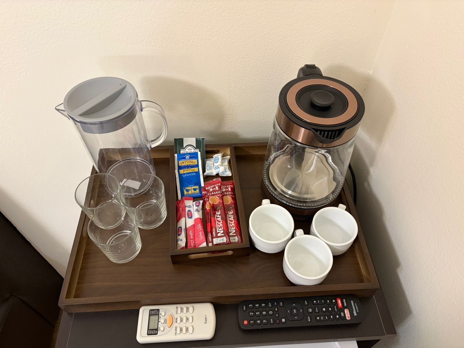 A tray with a coffee maker, coffee cups, a remote control, and a box of instant coffee.