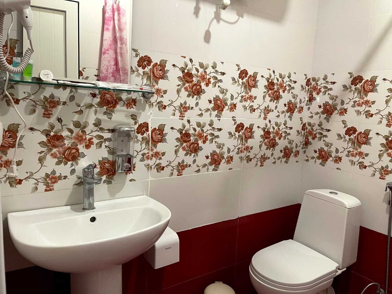 A bathroom with a floral tile backsplash, a white sink, and a toilet.