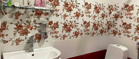 Un baño con detalles de azulejos florales, un lavamanos blanco y un inodoro.