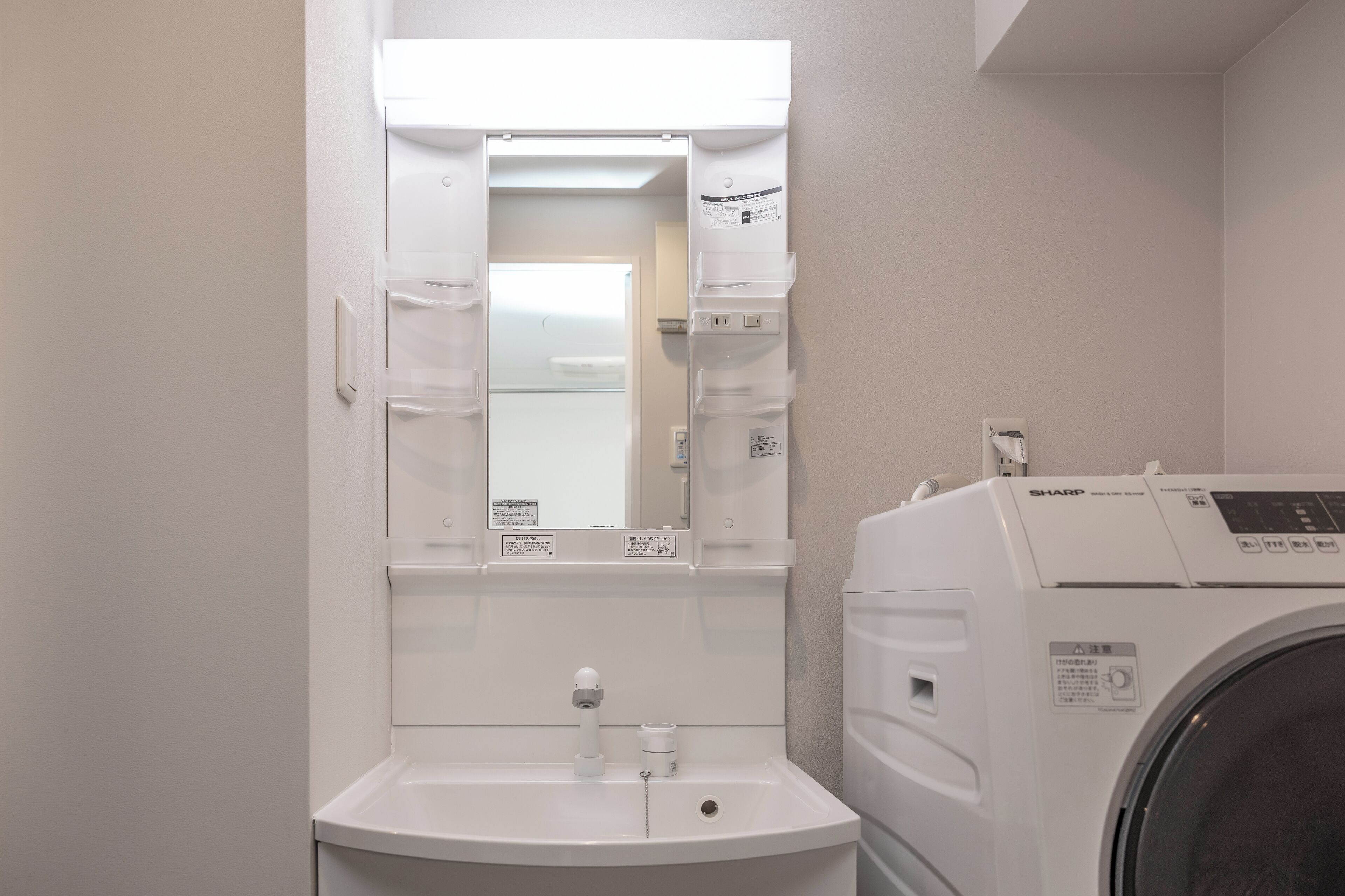 A compact bathroom with a sink, mirror, and a front-loading washing machine.