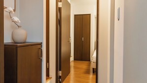 A hallway with a wooden cabinet and a vase with white flowers. There is a door at the end of the hallway. - BR KUJO - Self Check-In Only (Osaka)