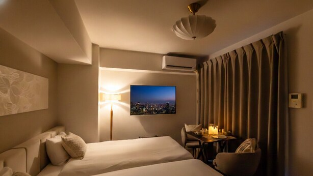 A hotel room with two beds, a desk with a chair, a lamp, a television, and a view of a cityscape. - BR KUJO - Self Check-In Only (Osaka)