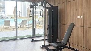 Ett gym med en bänk, en styrketräningsmaskin och utsikt över en simbassäng och ett utomhusområde.