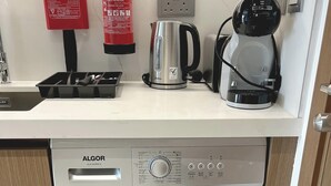 Ett kompakt kök med diskmaskin, kaffebryggare, vattenkokare och brandsläckare.