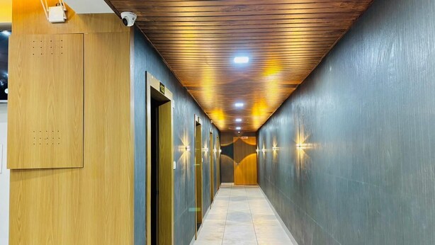 A hallway with wooden paneling on one side and a tiled floor, leading to a door at the end. - HOTEL HUNTER  (Bardoli)