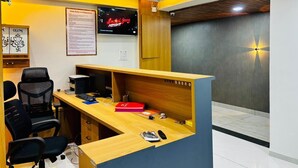 A hotel reception desk with a computer, chairs, and a wall-mounted TV displaying 'Hotel Rules and Regulation'. - HOTEL HUNTER  (Bardoli)