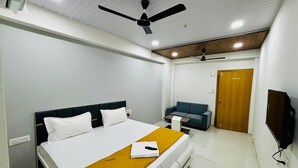 A hotel room with a bed, a sofa, a TV, and a ceiling fan. - HOTEL HUNTER  (Bardoli)