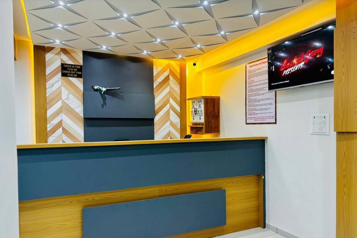 A hotel reception area with a modern design, featuring a check-in/out desk, a television displaying a movie, and a signboard with hotel information.