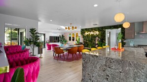 Eine moderne Küche mit einer Granitabdeckung, ein Essbereich mit Tisch und Stühlen sowie ein Wohnbereich mit leuchtend pinkfarbenen Sofas.