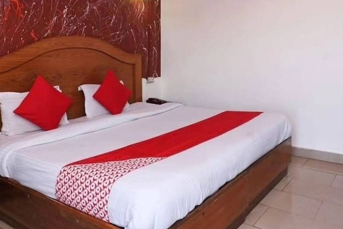 A hotel room with a wooden headboard, a bed with white and red bedding, a red throw blanket, and a wall with a marble-like texture.