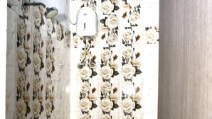 A bathroom with a toilet, a shower, and a wall with a floral tile pattern. - hotel Zinn satna (Satna)