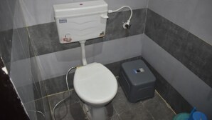 A small, tiled bathroom with a white toilet, a grey trash bin, and a wall-mounted electrical outlet. - hotel Zinn satna (Satna)