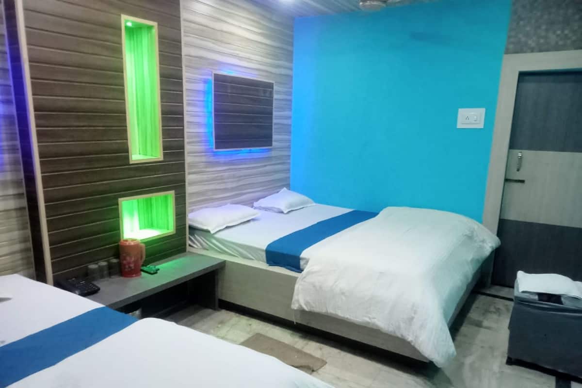 A hotel room with two beds, a nightstand, and a wall with a green-lit panel.