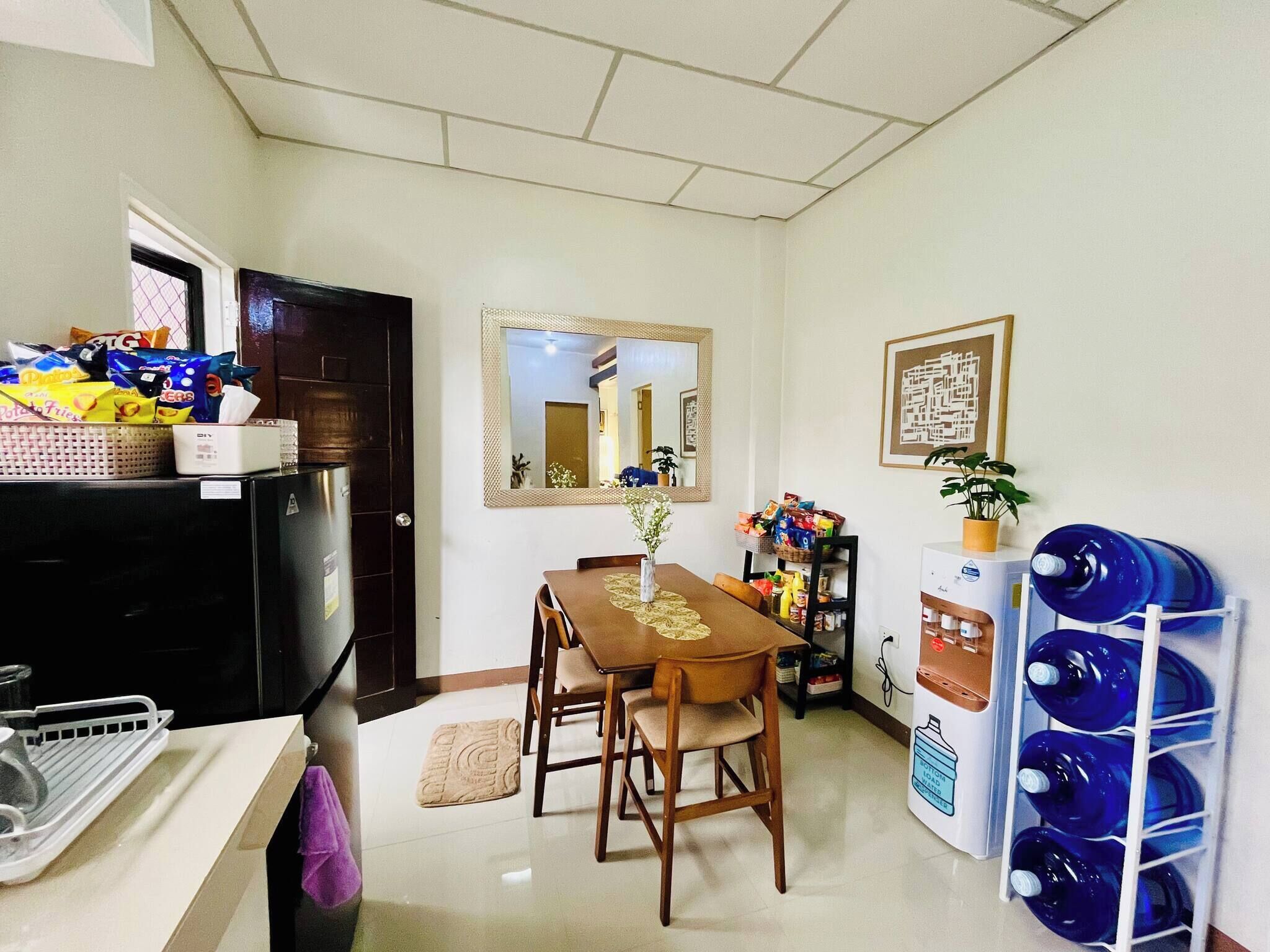 Una cocina compacta con refrigerador, una mesa de comedor con sillas, un dispensador de agua y una pequeña planta en maceta.