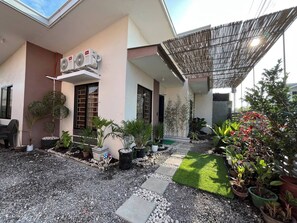 Una casa moderna con un porche cubierto, mobiliario exterior y una variedad de plantas en macetas.