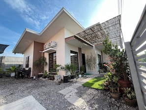 Una casa moderna con porche cubierto, mobiliario exterior y una variedad de plantas en macetas.