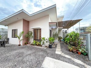 Una casa moderna con camino de grava, plantas en macetas y un pequeño patio.