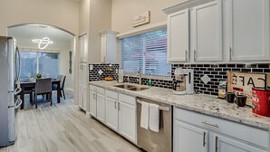Una cocina moderna con armarios blancos, salpicadero blanco y negro y un comedor con mesa y sillas.