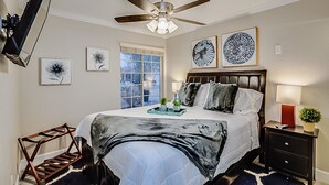 Un dormitorio con cama, ventilador de techo, ventana y obras de arte en las paredes.