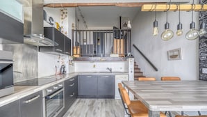 Et moderne køkken med stålemmer, et træspisebord og en trappe til et øvre plan.