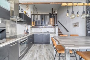 A modern kitchen with stainless steel appliances, a wooden dining table, and a staircase leading to an upper level. - Beachfront apartment with direct beach access (Arcachon)