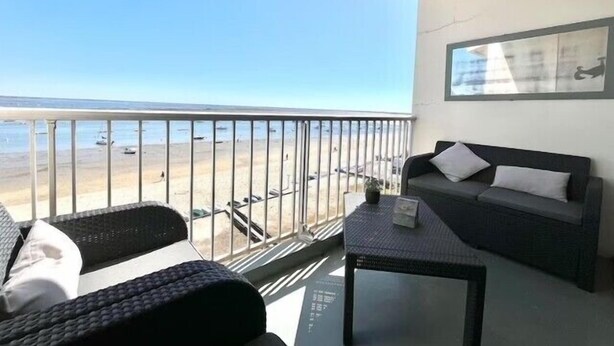 En balkon med udsigt over stranden, en sofa og et lille bord.