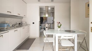 Een moderne keuken met witte kasten, een inbouwoven en een eethoek met een witte tafel en stoelen.