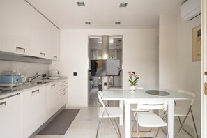 A modern kitchen with white cabinets, a built-in oven, and a dining area with a white table and chairs. - Two-room apartment in Forte dei Marmi Centro (Forte dei Marmi)