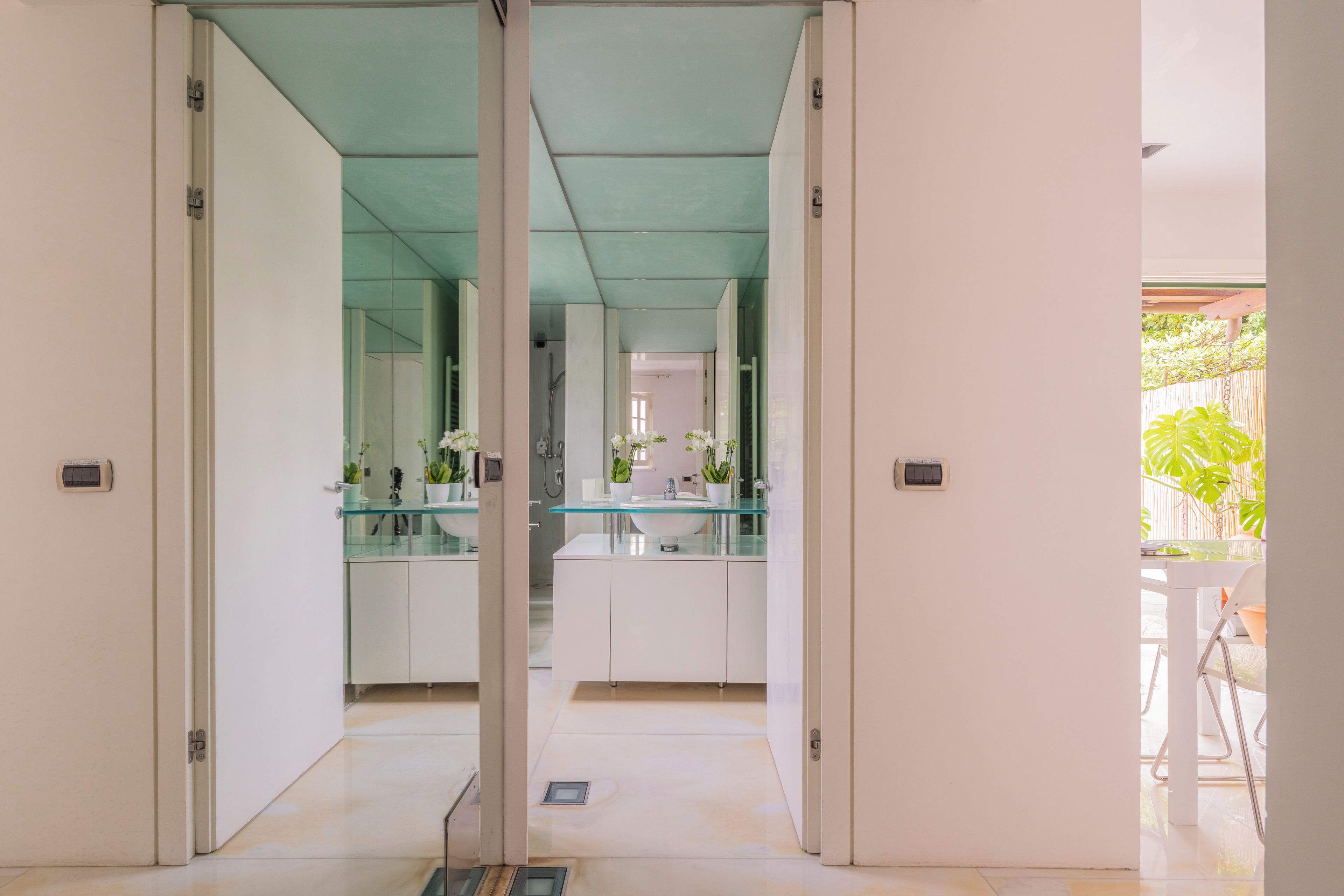 A modern kitchen with glass countertops, white cabinets, and a view of the outdoor area.