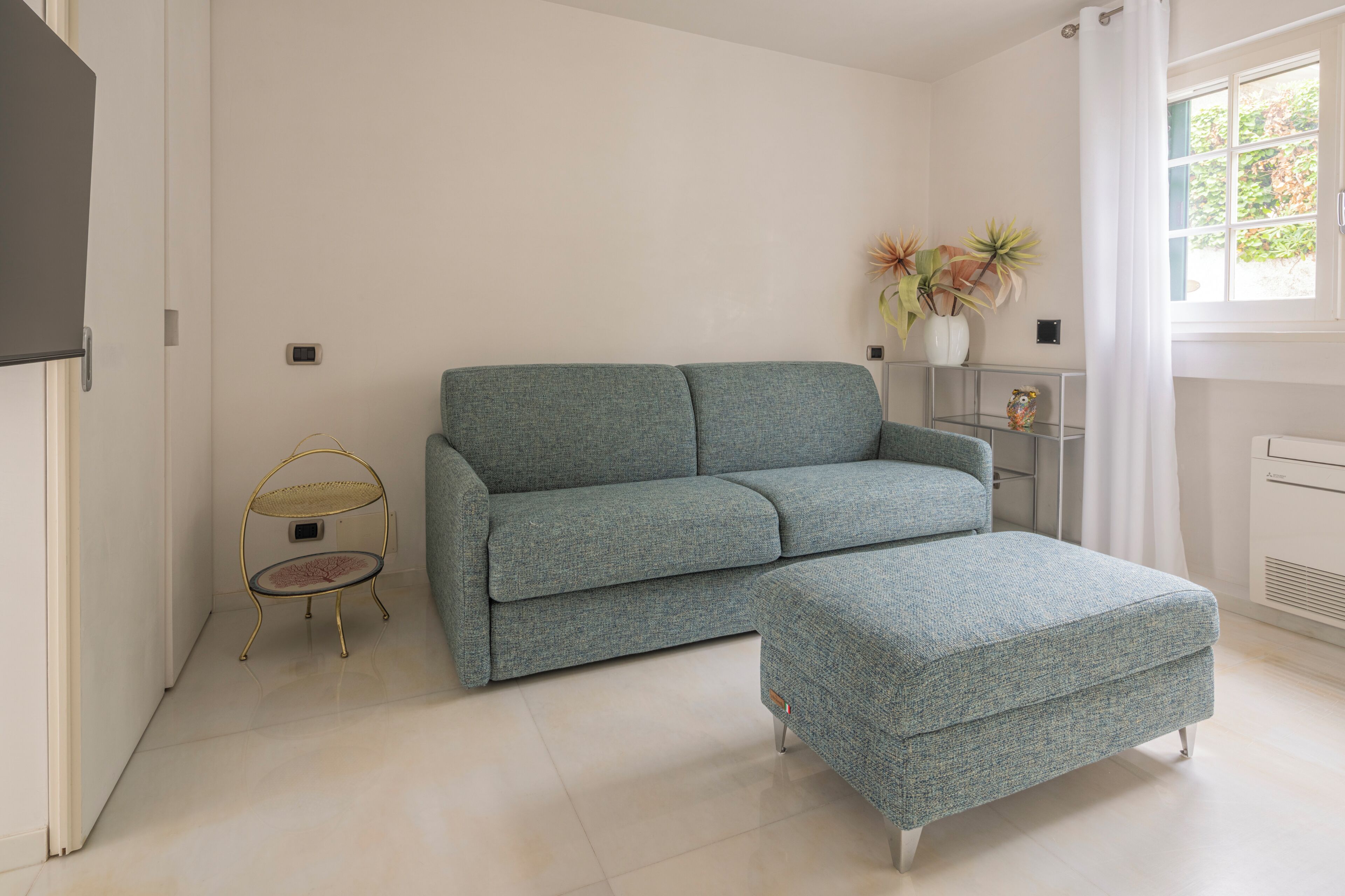 A living room with a sofa, ottoman, and a small table with a decorative item.
