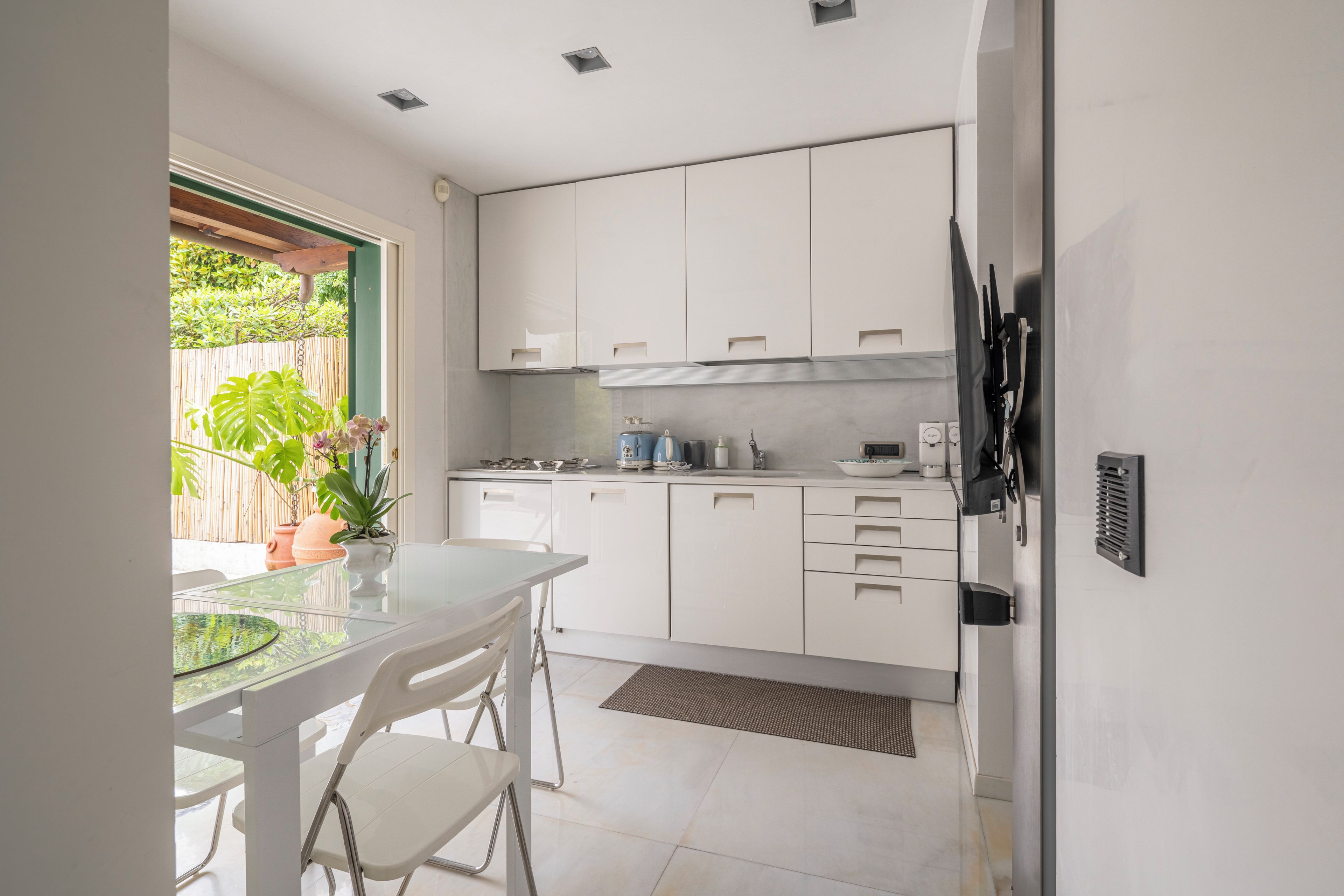 Een moderne keuken met witte kasten, een glazen tafel en een potplant.