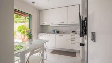Een moderne keuken met witte kasten, een glazen tafel en een potplant.