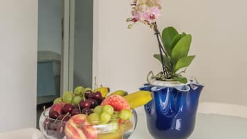 A fruit bowl with grapes, apples, and bananas on a table with a blue vase and an orchid.