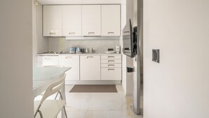 Een moderne keuken met witte kasten, een eettafel en een koelkast.