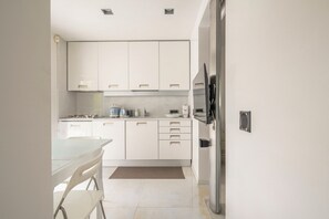 A modern kitchen with white cabinets, a dining table, and a refrigerator. - Two-room apartment in Forte dei Marmi Centro (Forte dei Marmi)