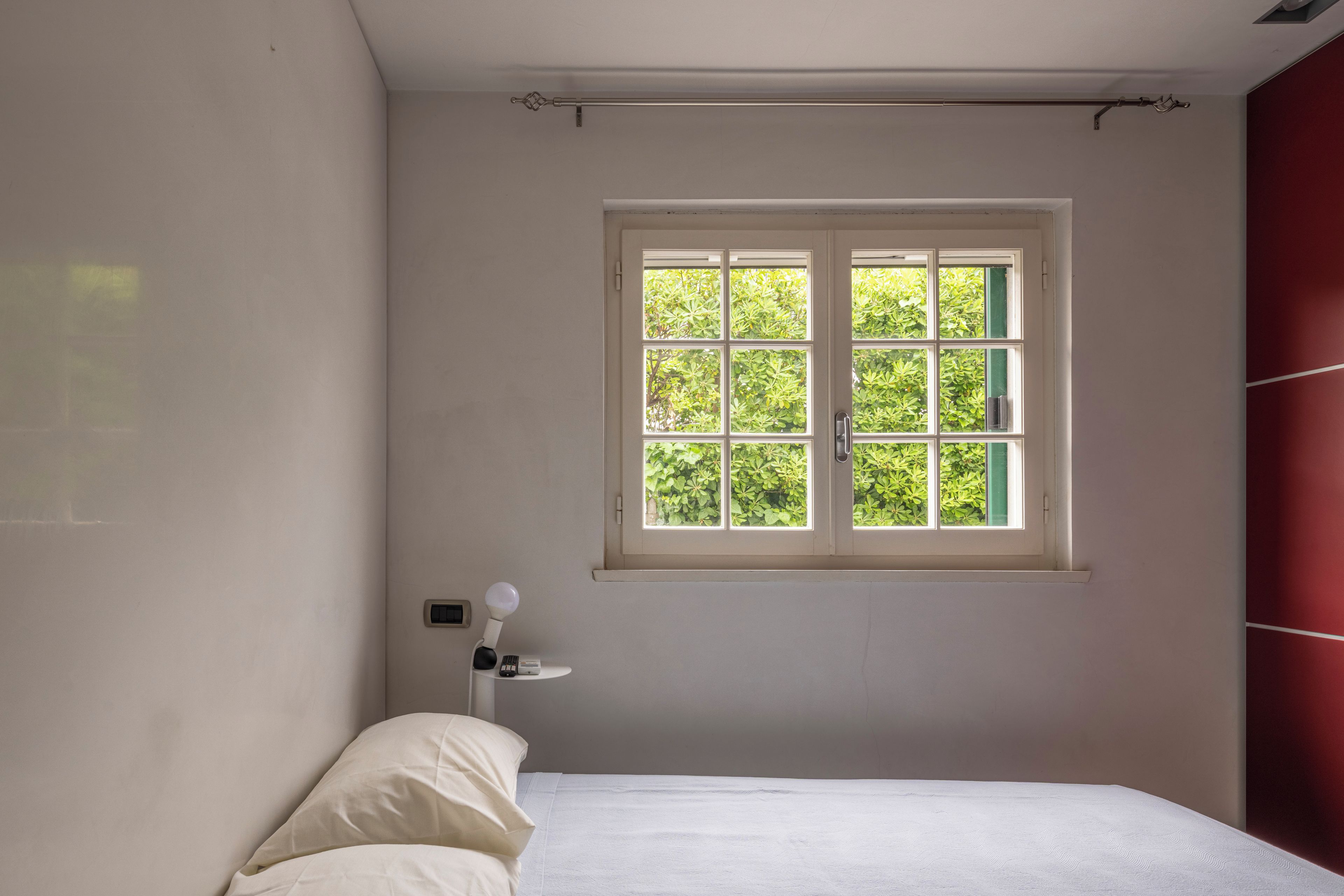 A bedroom with a bed, a window, and a nightstand with a lamp.