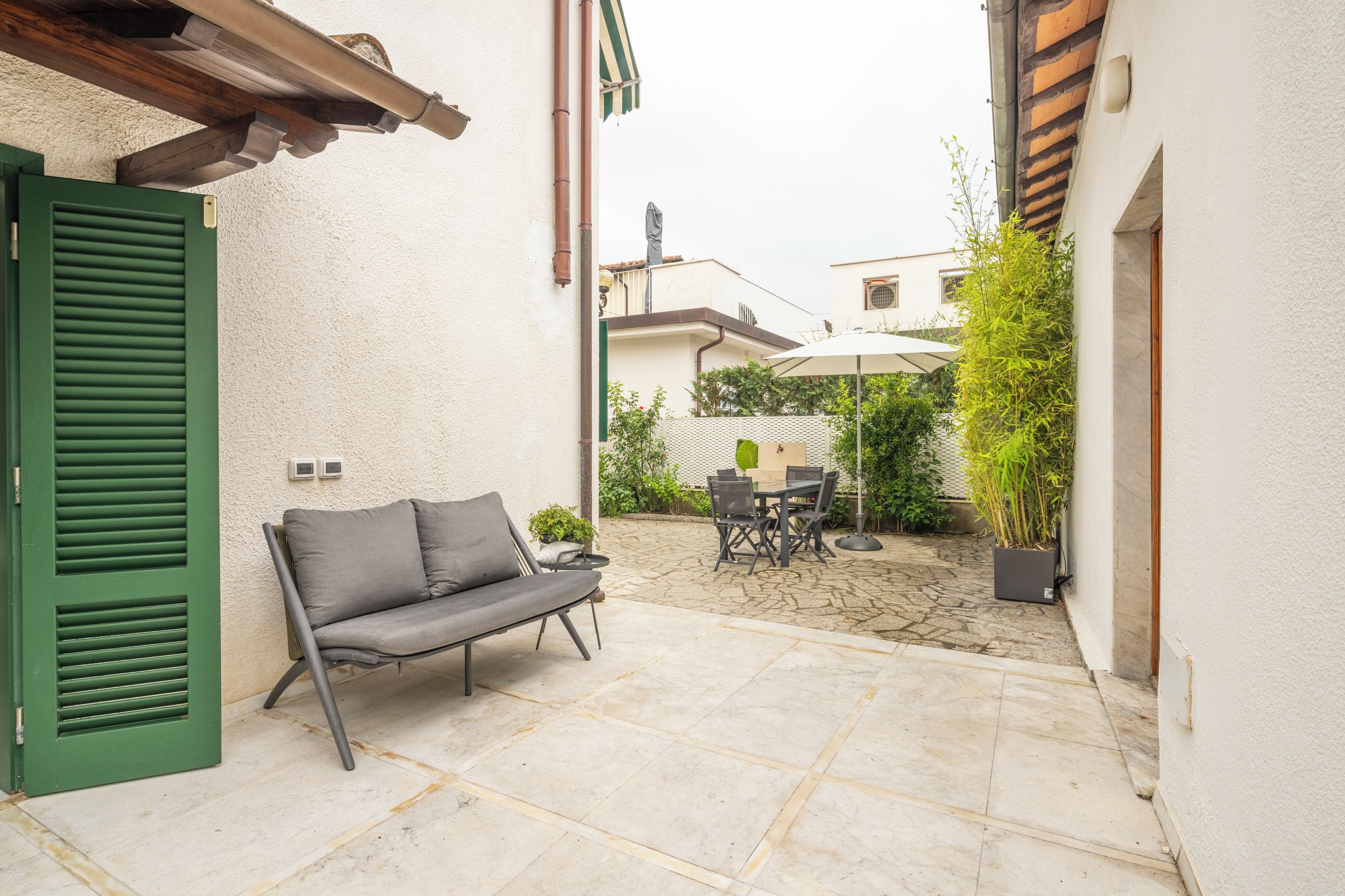 An outdoor patio with a sofa, table, chairs, and a potted plant.