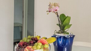 Een schaal met druiven, appels en bananen op een tafel, samen met een blauwe vaas en een orchidee.